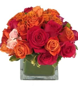 This design is HOT. Full of orange, hot pink, and pink roses and spray roses designed in a leaf wrapped glass cube that will heat up any space!