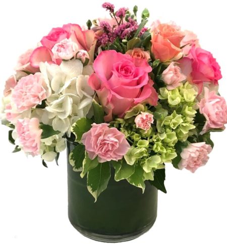 This bouquet features spring pastel colored roses, spray roses, and mini carnations in a bed of white and green hydrangea, accented with limonium and variegated pittosporum.