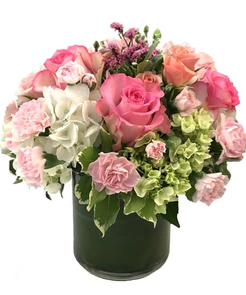 This bouquet features spring pastel colored roses, spray roses, and mini carnations in a bed of white and green hydrangea, accented with limonium and variegated pittosporum.