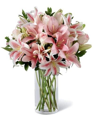 handcrafted by an artisan florist of pink roses and pink Asiatic lilies enhanced with lush greens is arranged in a clear glass cylinder vase